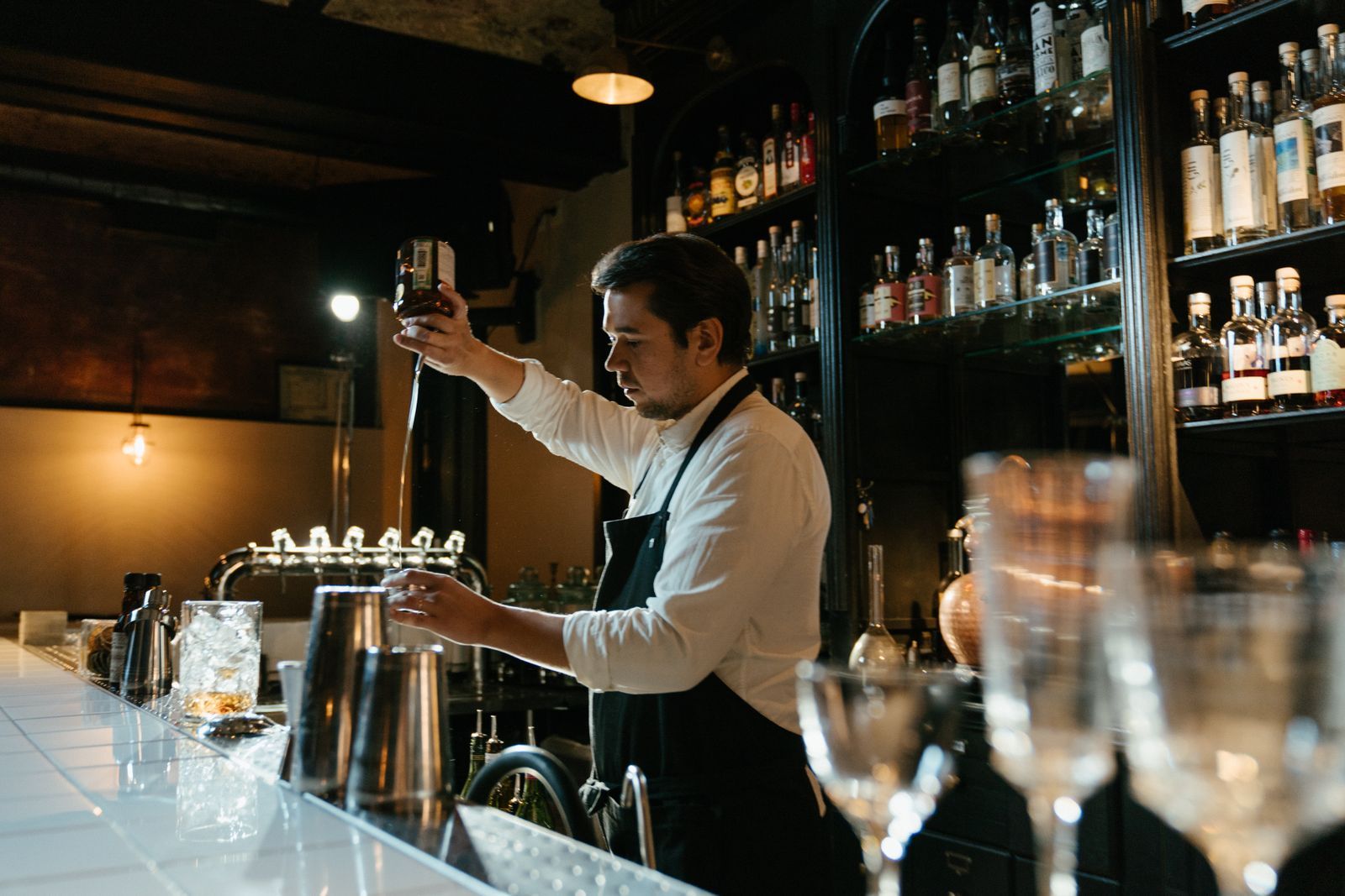 A bartender making a drink behind a dark timber bar